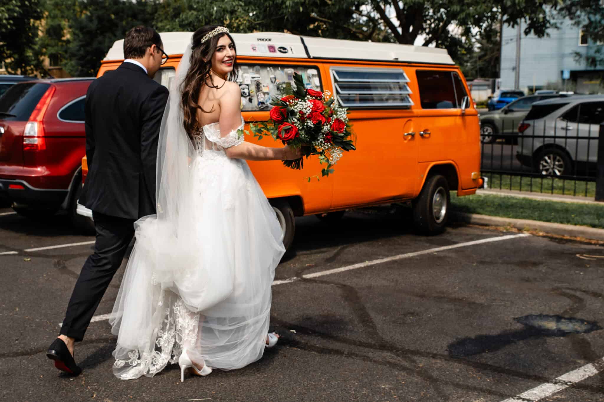 Elegant wedding couple standing near vibrant orange vintage van, capturing wedding photography moments.