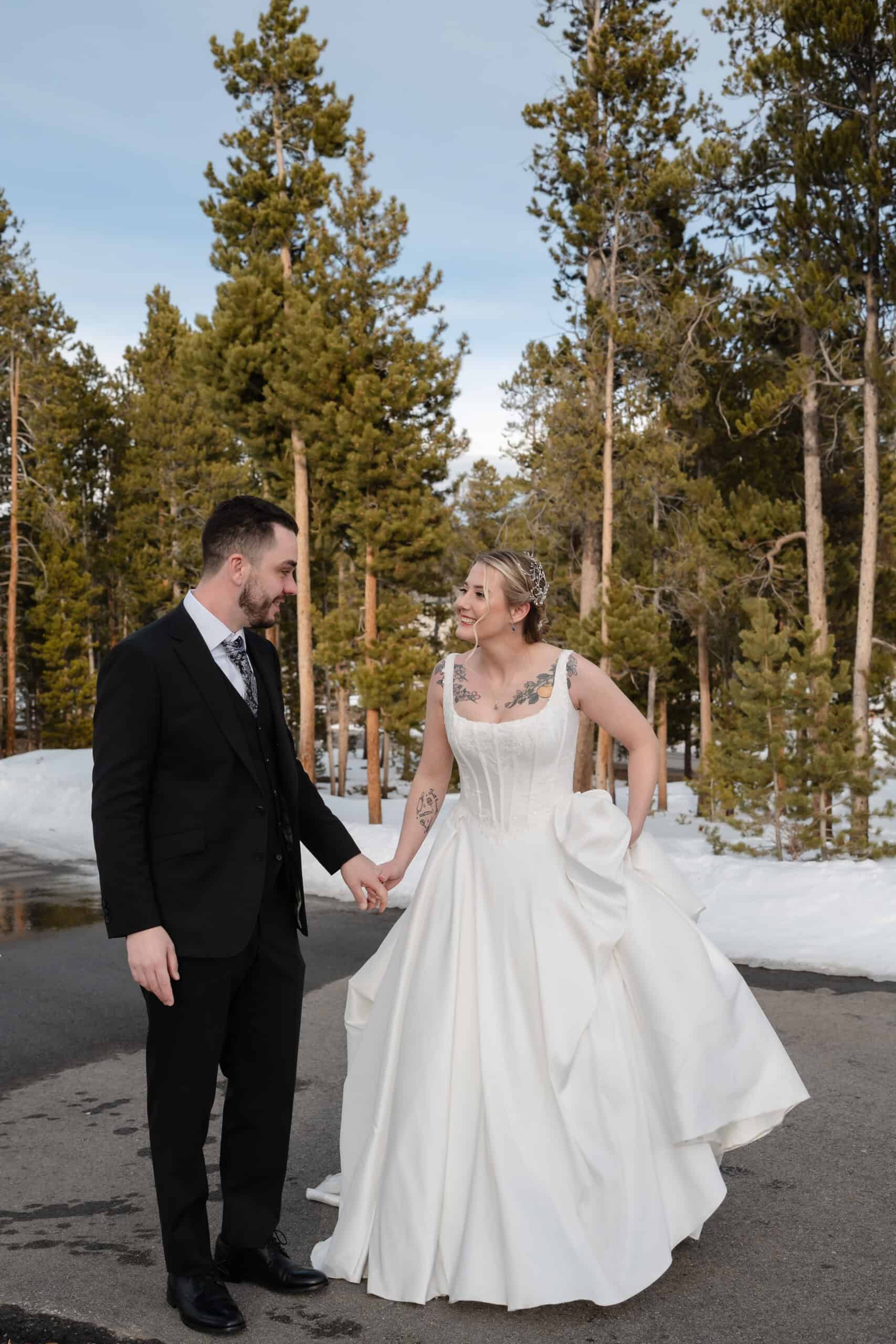 Wedding couple holding hands outdoors in winter forest setting, celebrating love and unity.